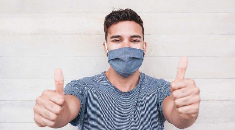 young man wearing a mask smiling and giving two thumbs up