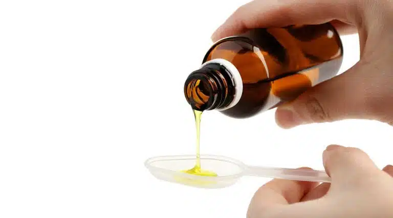 woman pouring a yellow liquid into a spoon Tussionex Cough Syrup
