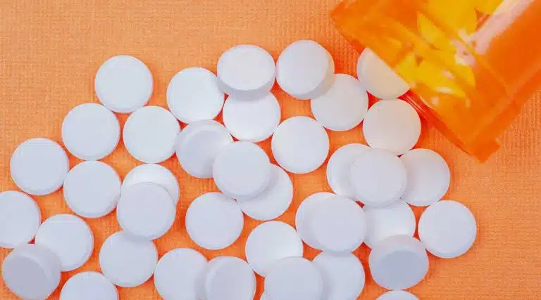 orang pill bottled spilled across an orange table with round pills spread across orange table