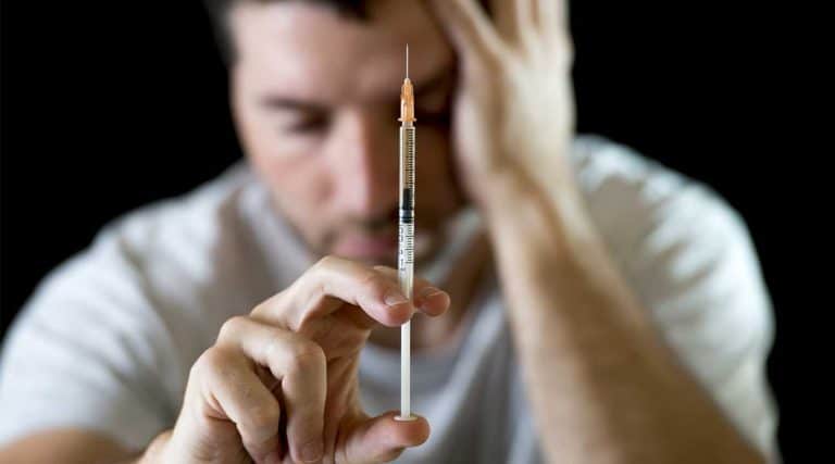 young man holding a syringe injecting cocaine