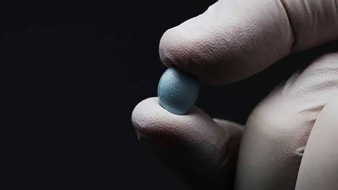 doctor holding a small blue pill - Halcion Side Effects, Warnings, & Drug Interactions