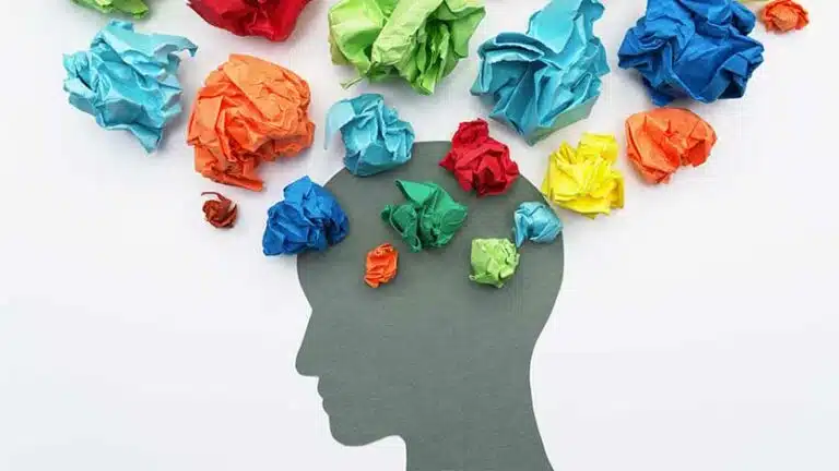 Image of the silhouette of a head surrounded by colorful crumbled pieces of paper used to demonstrate a persons thoughts - Types Of Mental Health Disorders